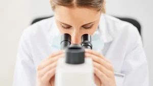 Scientist in white lab coat using a binocular microscope, representing pharmaceutical and laboratory research solutions from SBR International GmbH