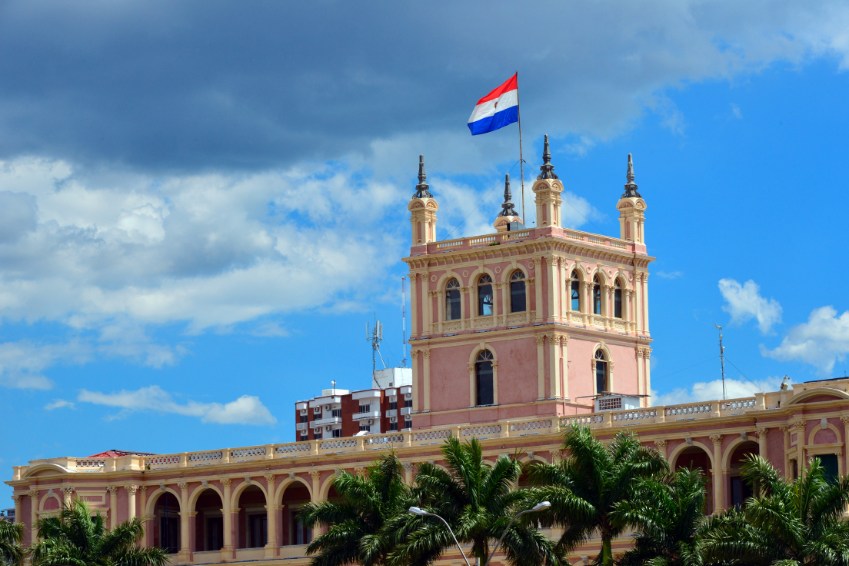 Historic government building in Asunción, Paraguay with national flag and palm trees, symbolizing culture and heritage