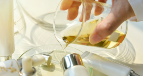 Cosmetic formulation with yellow liquid poured into container, surrounded by skincare product bottles, symbolizing beauty innovation