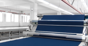 Large roll of blue fabric being processed in a textile manufacturing facility, symbolizing raw materials and fabric production