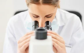 Scientist in white lab coat using a binocular microscope, representing pharmaceutical and laboratory research solutions from SBR International GmbH
