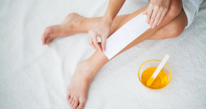 Person applying waxing strip on leg with bowl of wax and spatula, symbolizing beauty, personal care, and hair removal